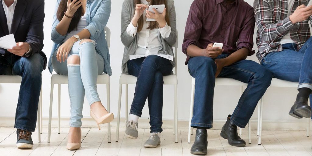 Customers seated in a waiting room using their mobile phones.