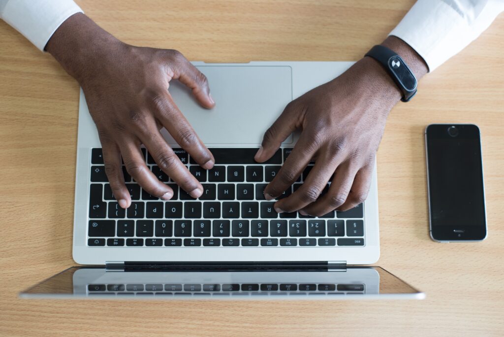 Overhead view of a laptop and smartphone with hands typing on the keyboard.