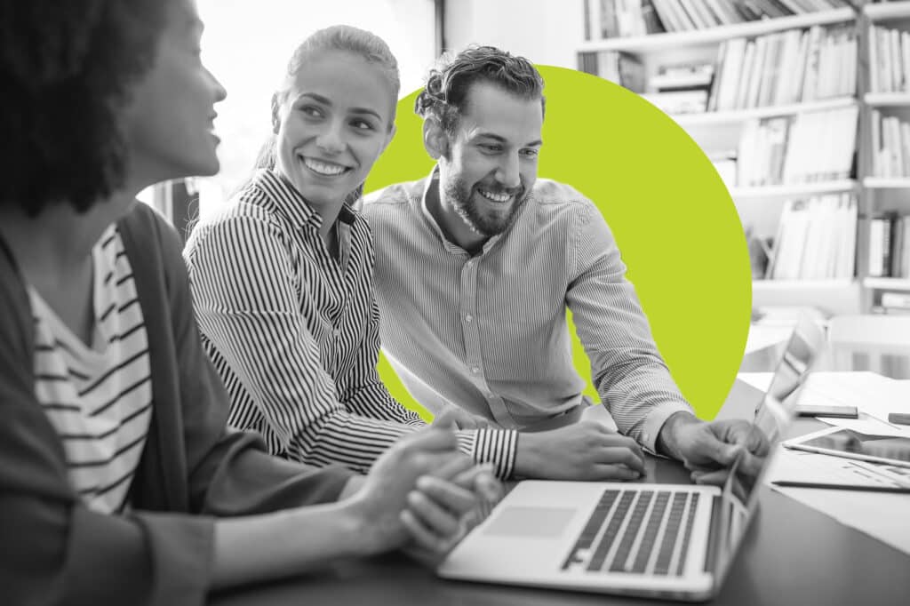 A group of coworkers huddles over a laptop with a branded yellow bubble behind them to illustrate digital advertising terms