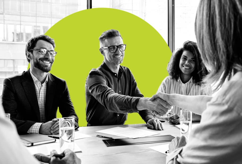A diverse group of sales people shake hands across a conference table with a marketer.