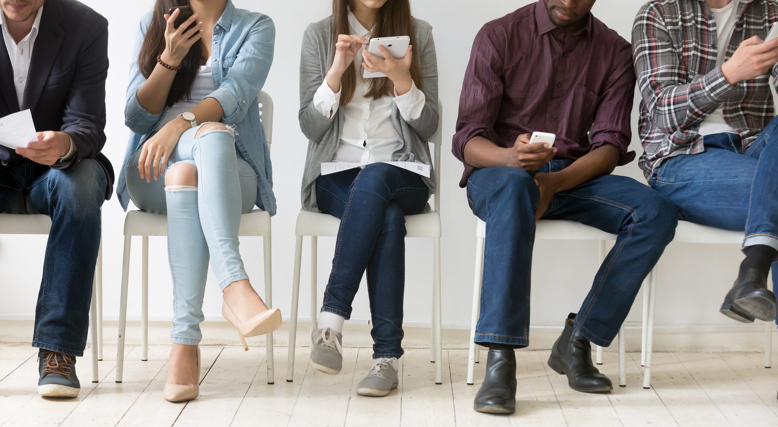 People sitting in a waiting room receiving SMS messages on their mobile devices.